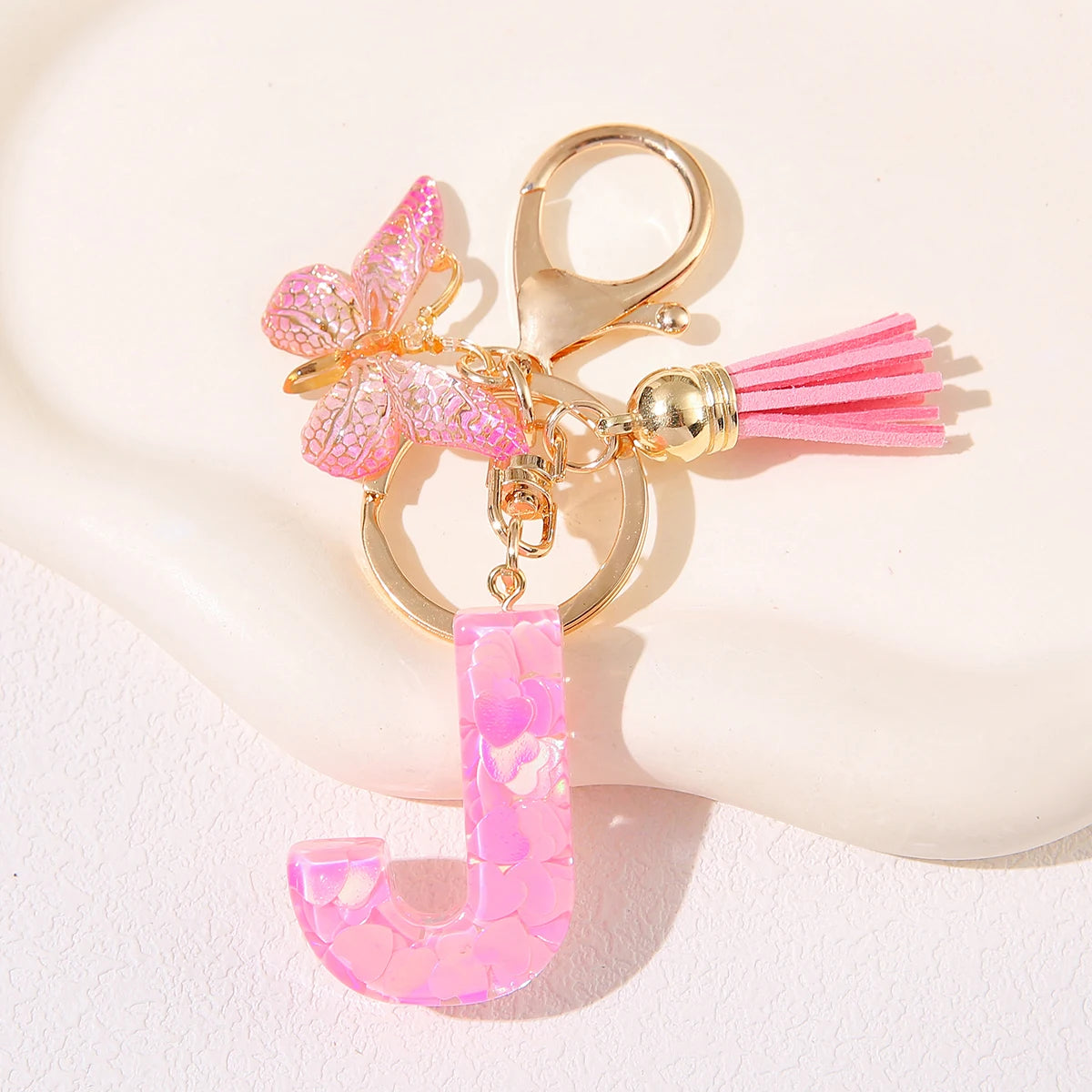 A gold initial heart keychain featuring a pink butterfly charm and a pink tassel.