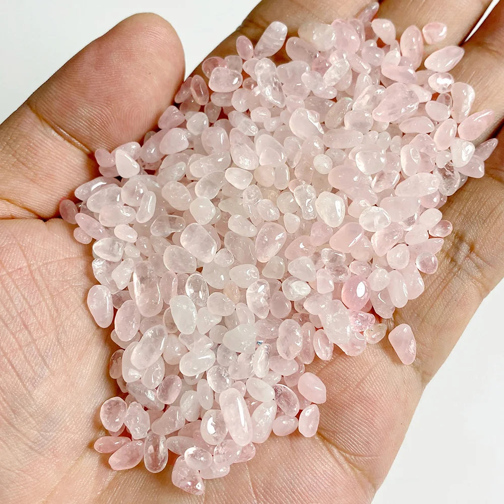 A hand holds a pile of clear pink rose quartz tumbled stone chips for jewelry making