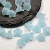 Light blue frosted acrylic flower beads scattered on a dark stone surface
