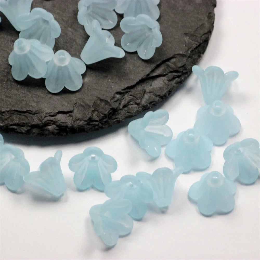Light blue frosted acrylic flower beads scattered on a dark stone surface