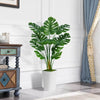 A vibrant green faux monstera palm plant in a white pot displayed on a wooden cabinet.