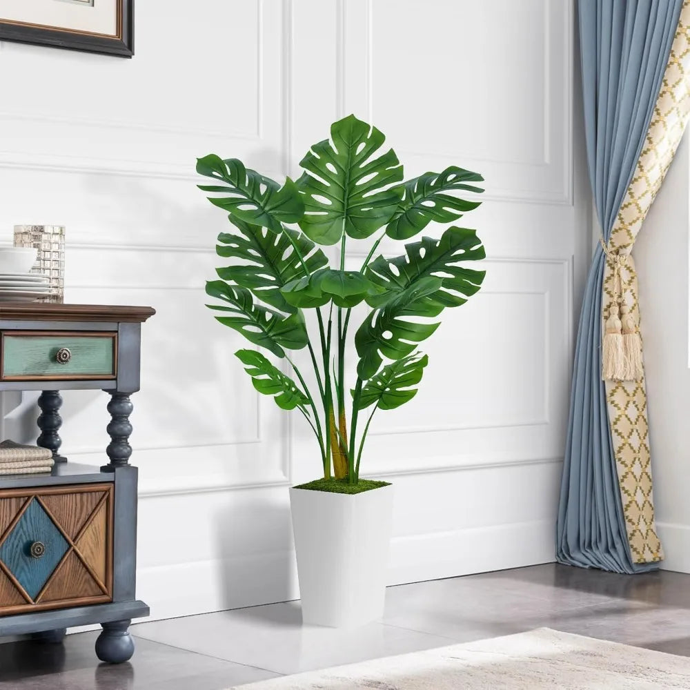 A vibrant green faux monstera palm plant in a white pot displayed on a wooden cabinet.