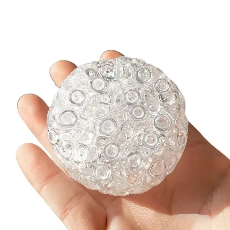 A hand holds a clear, spherical fidget ball made of soft, squeezable material.