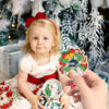 A young girl holds a diamond painting craft kit with a charm pendant and a small white figurine in front of a snowy Christmas