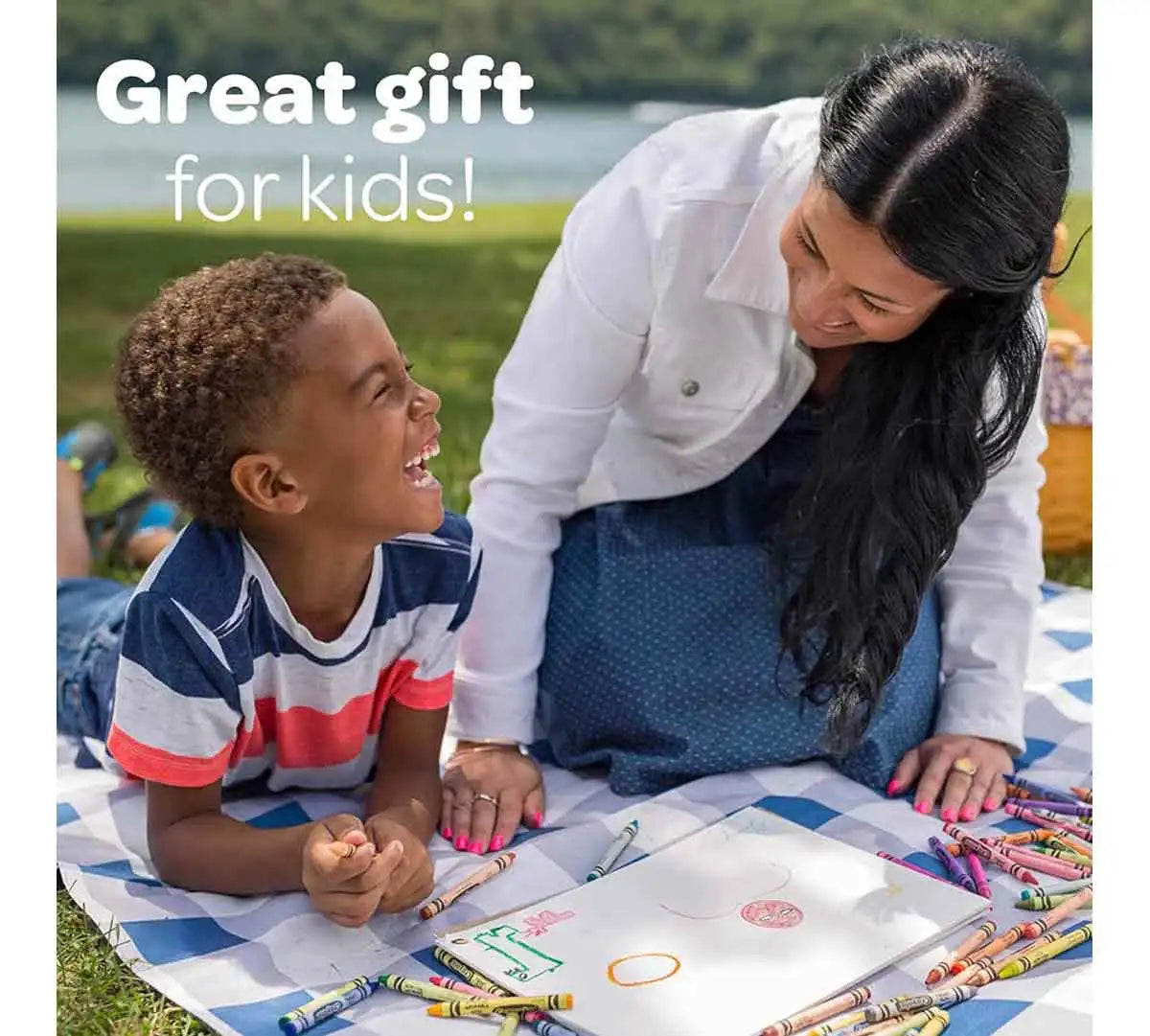 A woman is helping a young boy color on a sheet of paper with jumbo washable crayons outdoors.