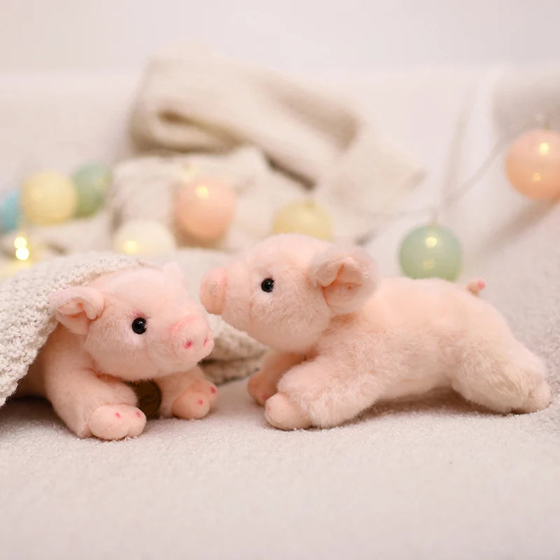 A small, pink plush pig stuffed animal lying on a white surface with soft fabric and decorative lights.