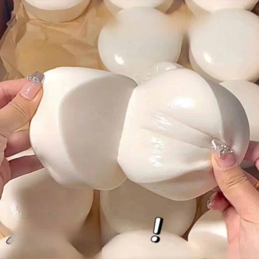 A hand is squeezing a white yogurt cake squishy stress relief toy against a light brown background.