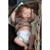 A newborn reborn baby doll with rooted hair sleeping inside a woven basket.
