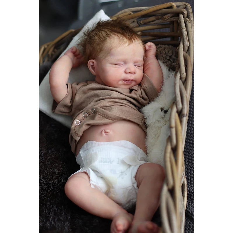 A newborn reborn baby doll with rooted hair sleeping inside a woven basket.