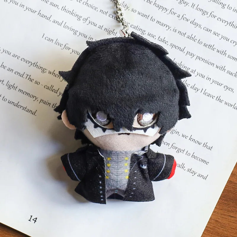 A plushie pendant charm of an anime character with black hair and white markings, resting on a piece of paper.