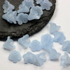 Small, translucent light blue frosted acrylic flower beads scattered on a dark stone surface.