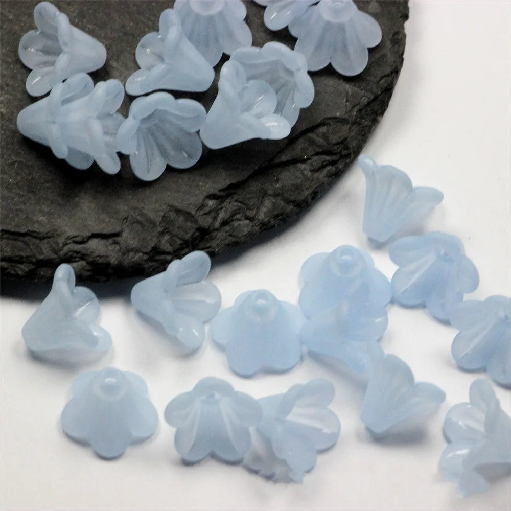Small, translucent light blue frosted acrylic flower beads scattered on a dark stone surface.