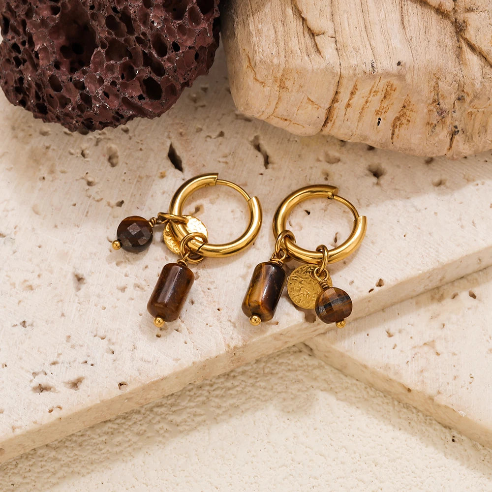 Gold hoop earrings featuring tiger's eye stones and gold accents resting on a light surface.