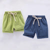 A pair of light green linen shorts with a drawstring waist and a pair of dark blue linen shorts with a drawstring waist.