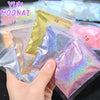 A hand holds several small plastic bags of holographic rainbow nail glitter for DIY nail art