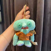 A light blue monster plush keychain with orange fabric accents being held by a hand.