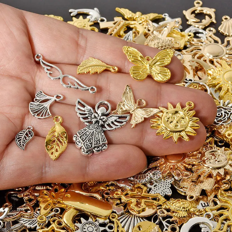A hand holds a collection of mixed metal charms, including gold and silver, for DIY jewelry making.