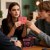 A woman and a man look at couples scratch-off challenge cards for romantic date nights on a wooden table.
