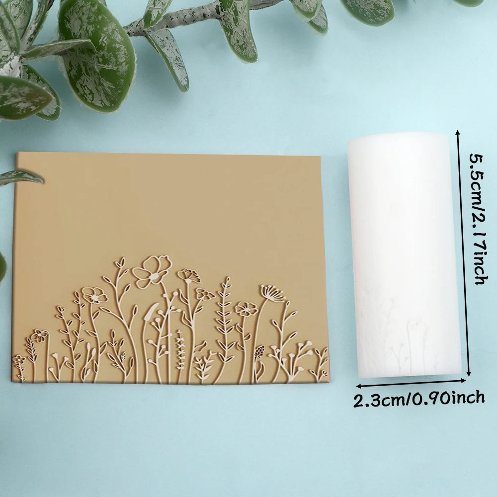 A light beige clay texture roller and a white candle are displayed on a light blue background with green foliage.