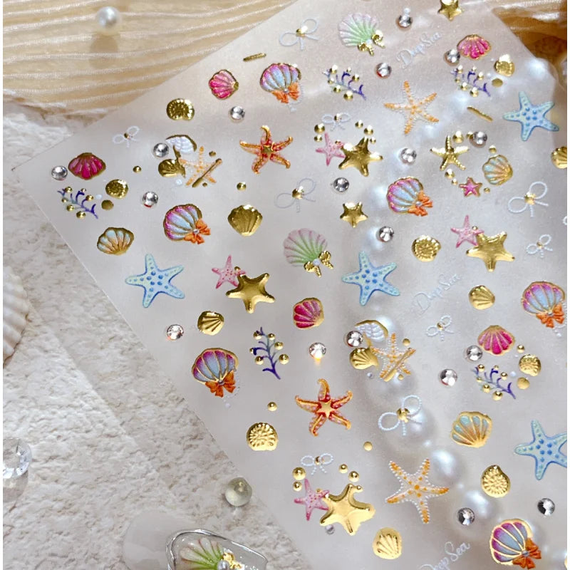 Clear sheet of 3D ocean-themed nail art stickers featuring gold and iridescent starfish and shell shapes
