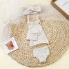 A knitted three-piece outfit set for a baby doll featuring a top, skirt, and bottoms, displayed on a woven mat.