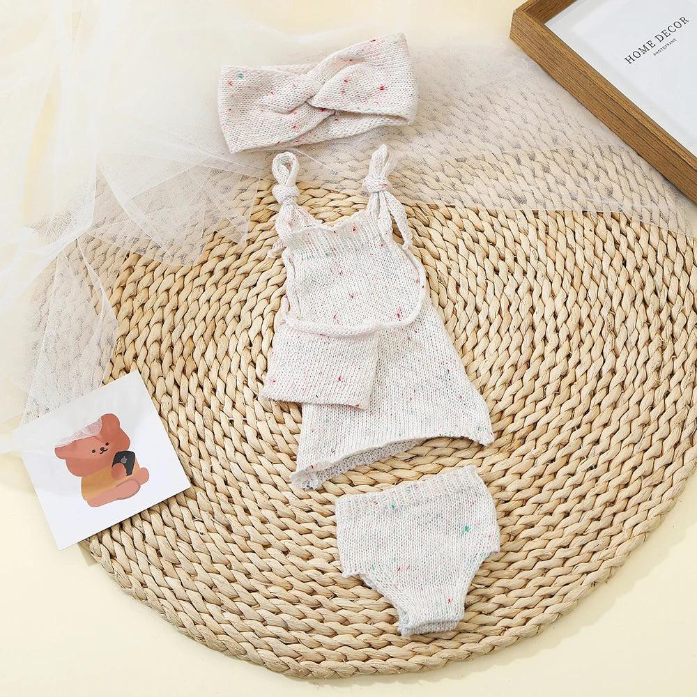 A knitted three-piece outfit set for a baby doll featuring a top, skirt, and bottoms, displayed on a woven mat.