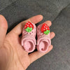 Pink fashion slippers with red strawberry decorations being held in a hand.
