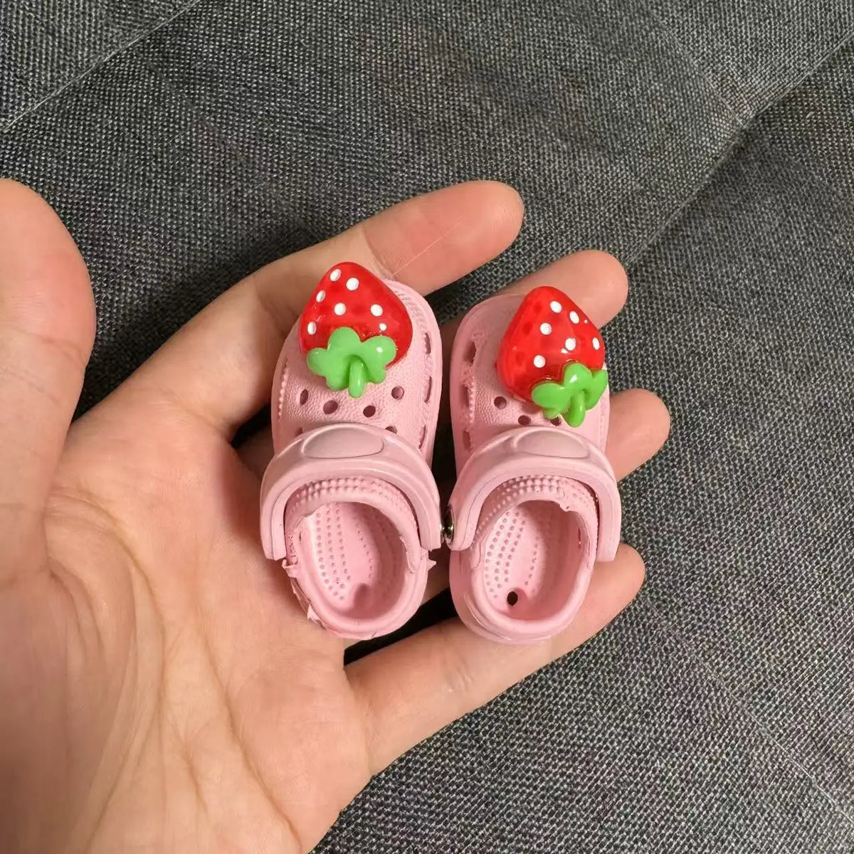 Pink fashion slippers with red strawberry decorations being held in a hand.