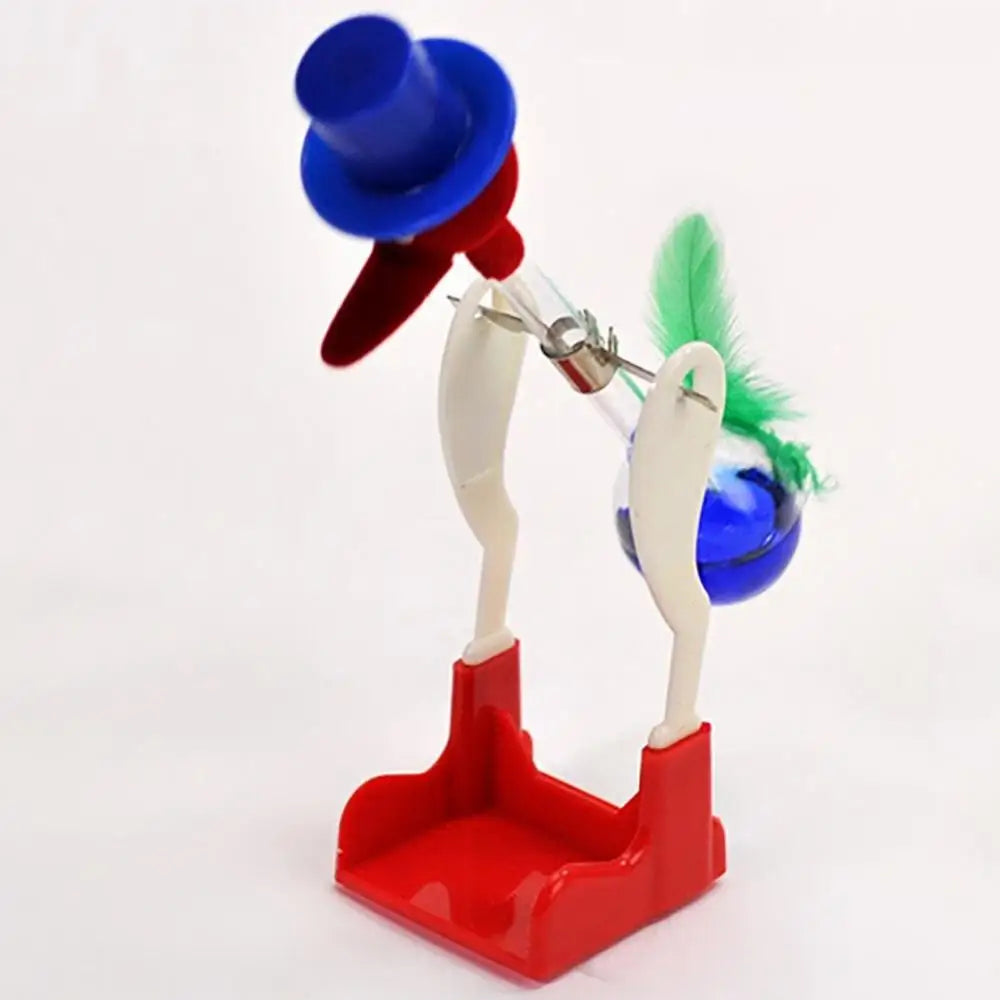 A red and blue drinking bird toy with a purple hat and green feather, designed for perpetual motion desk decor.