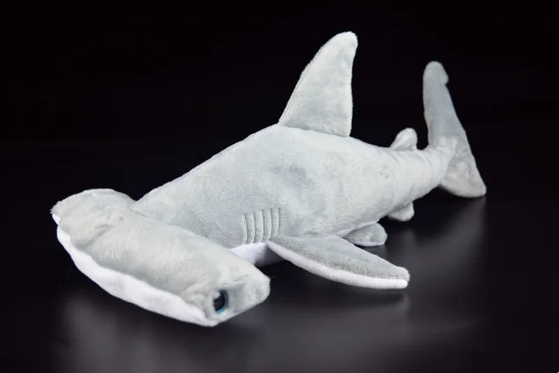 A soft gray hammerhead shark plush toy lying on a dark surface.