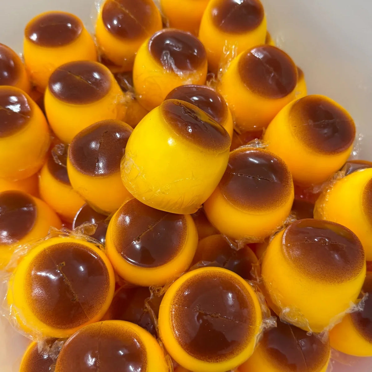 A close-up view of numerous orange and yellow squishy pudding stress balls in a white container.