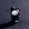 A small black and white cartoon bear figurine with pink accents sitting on a dark textured surface.