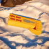 A yellow beach tools excavator toy lying on a snowy surface.