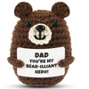 A brown crochet bear plush toy with a white snout and a sign that reads Dad you're my bear-illiant hero