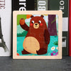 A wooden tangram puzzle featuring a cute brown bear surrounded by colorful nature elements.