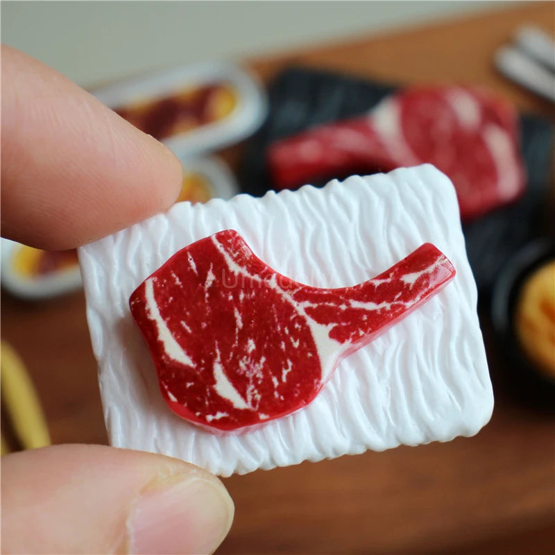 A hand holds a miniature dollhouse beef steak and pasta set toy food featuring a sliced red meat piece.