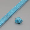 A close-up of a thin, blue glitter paper strip and a small piece of folded blue glitter origami star paper.
