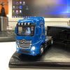A blue Mercedes Actros diecast container truck with pull-back action displayed on a black surface.