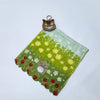 A green fabric item shaped like a landscape with small white flowers and red berries, featuring a small brown hippo plush toy
