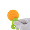A hand holds an orange silicone fruit-shaped baby teether with a green handle.