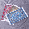 A stack of handwoven Turkish style miniature carpet mats featuring intricate blue, red, and beige patterns.