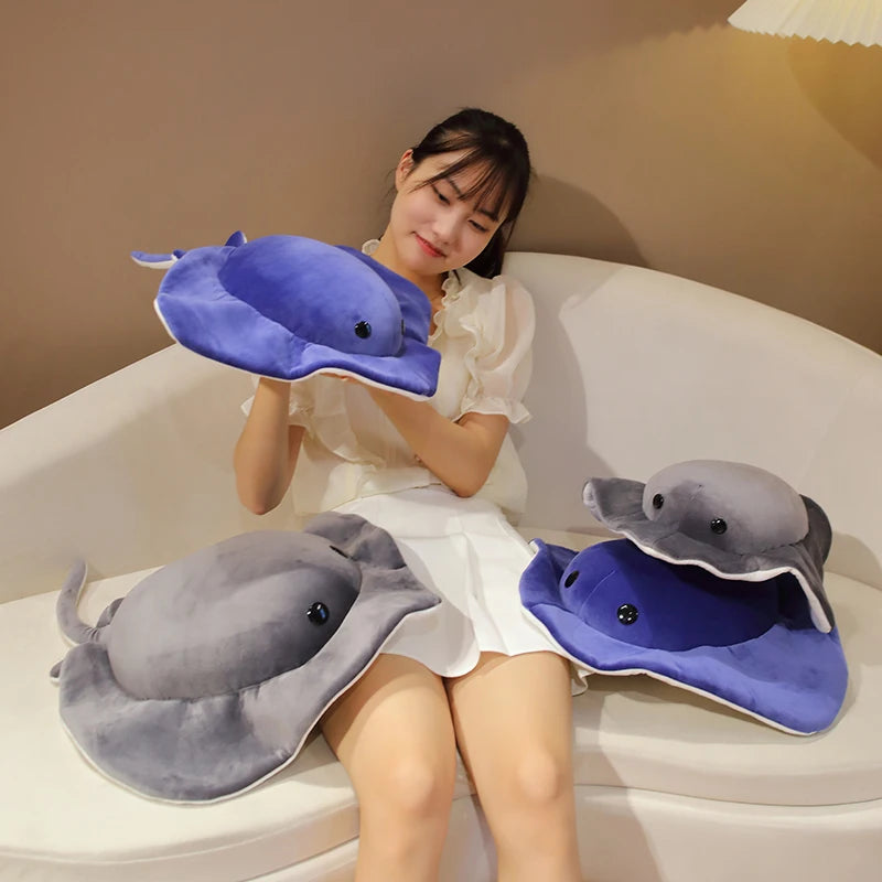 A young woman is sitting on a white sofa with two plush toy dolphins, one gray and one purple, resting on her lap.