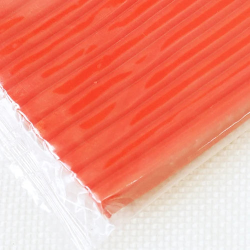 A close-up view of a rectangular block of soft, translucent orange polymer clay modeling material.