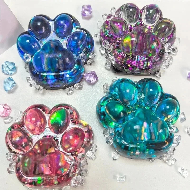 A collection of iridescent, purple, and blue cat paw squishy fidget toys with sparkling accents.