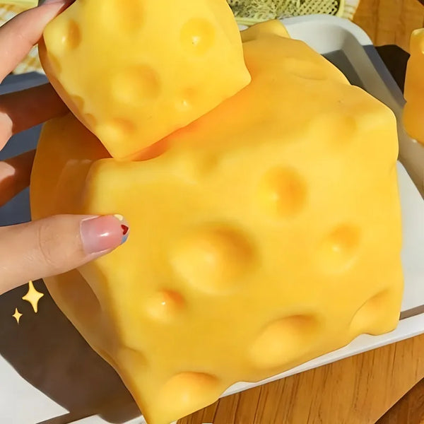 A bright yellow giant squeeze cheese fidget toy is held by a hand and placed on a white plate.