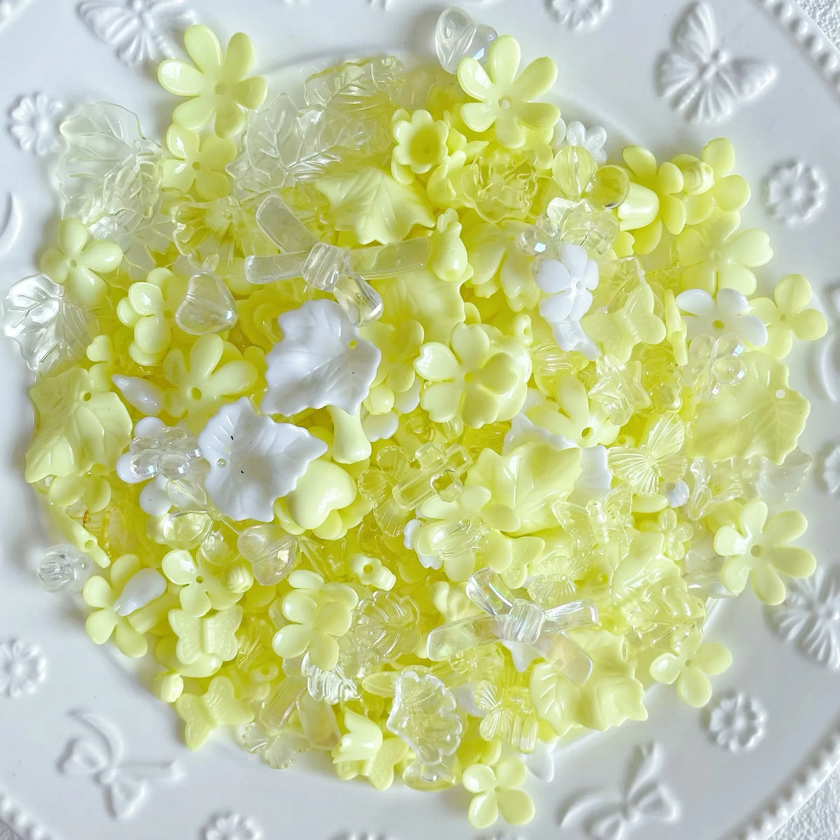 A pile of yellow and white acrylic bow and flower beads for DIY jewelry making