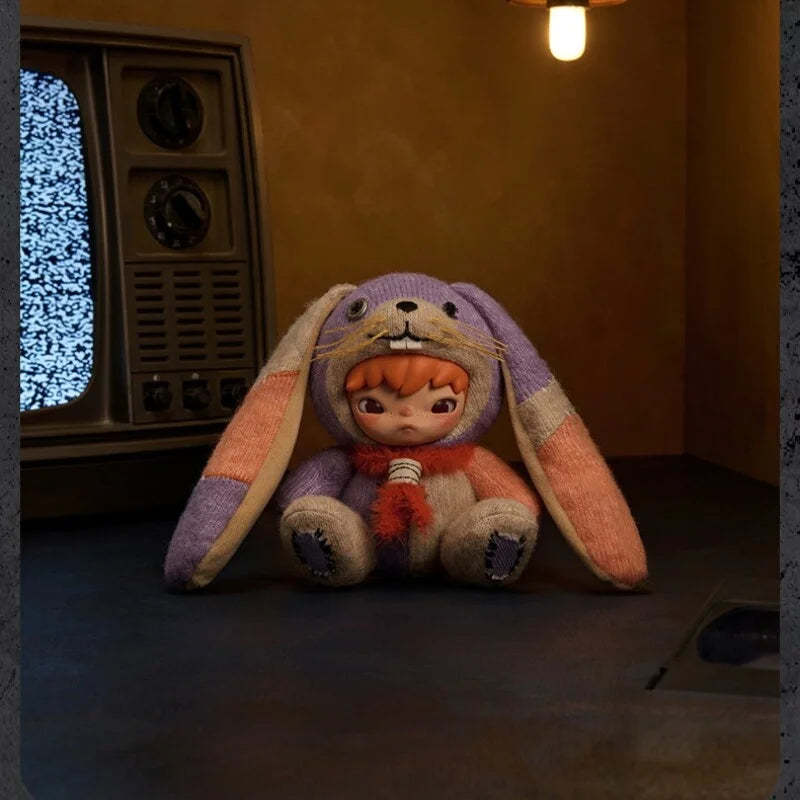 A purple and orange plush doll with long floppy ears is displayed in a dimly lit room.