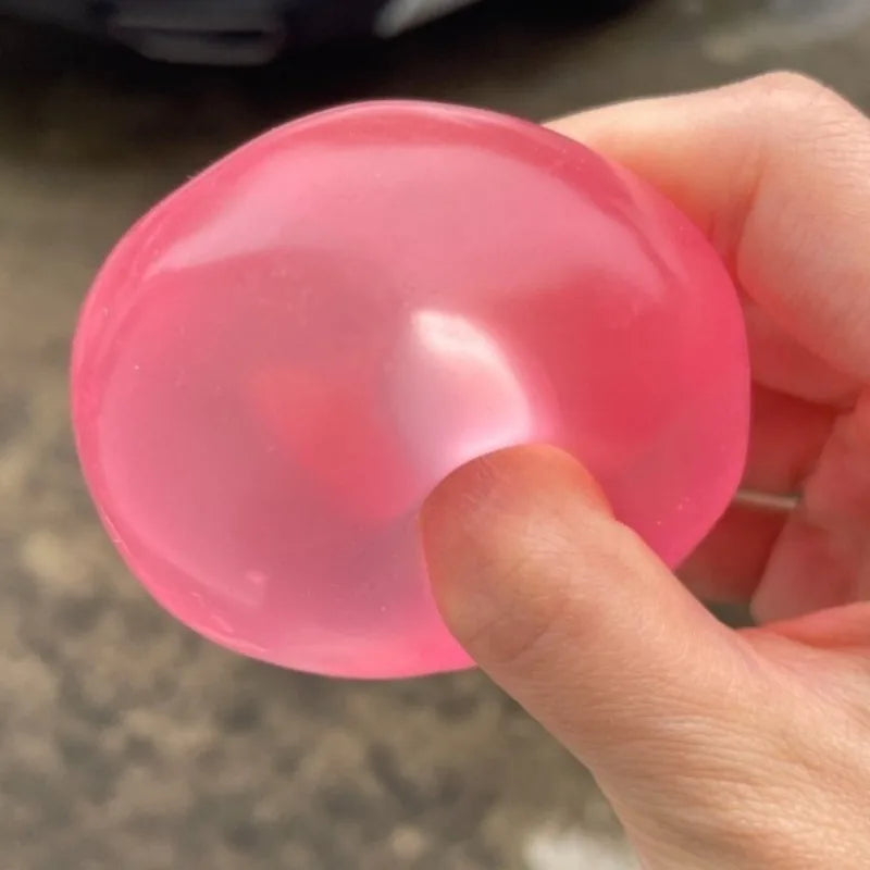 A hand holds a translucent pink moldable squishy stress relief toy, showing its smooth, rounded shape.