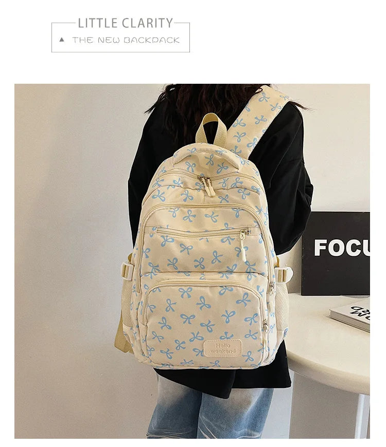 Sac à dos à nœud bleu clair et blanc porté par une personne contre un mur blanc.