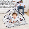 A baby corral fitness stand with a play mat and hanging toys is shown on a white rug.